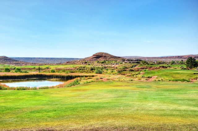 Golf course fairway and pond beneath a desert mesa