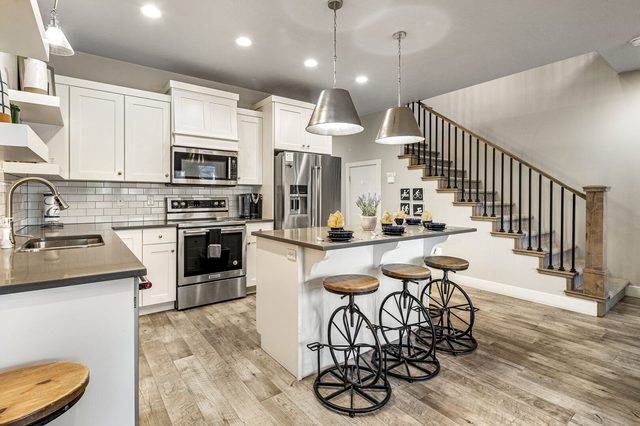 White kitchen with stainless appliances, island stools and staircase