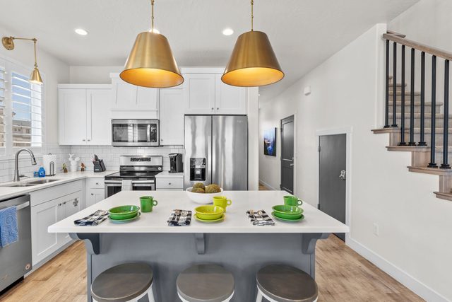 White kitchen with island seating, stainless appliances and stairs
