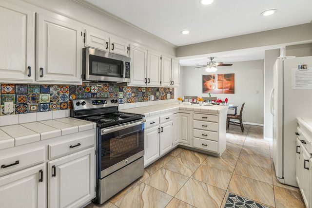 Kitchen with white cabinets, stainless range and colorful tile backsplash
