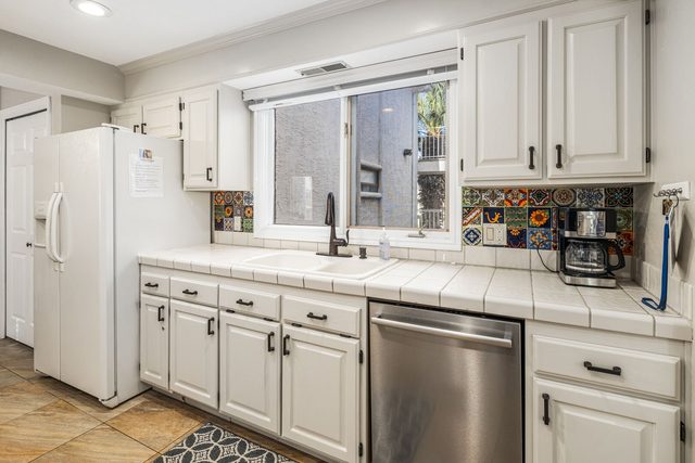 Kitchen sink under window with dishwasher and white refrigerator
