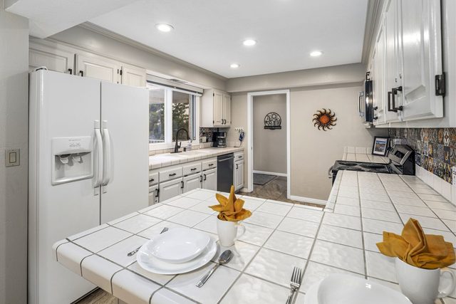 Tiled kitchen counter set with plates beside white side-by-side refrigerator