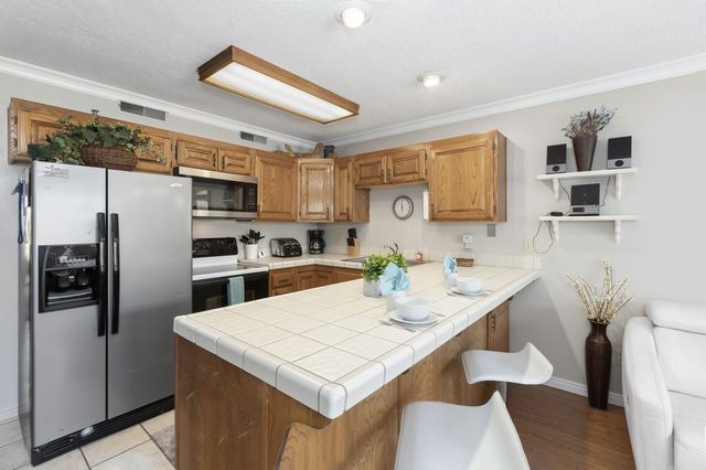 Kitchen with stainless refrigerator and tiled peninsula bar seating