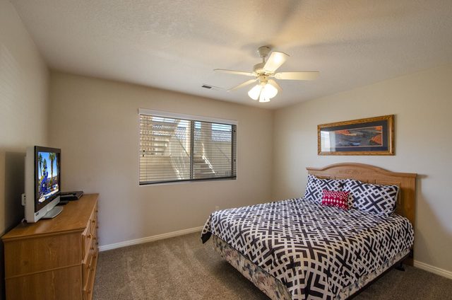 Bedroom with wood headboard, ceiling fan and dresser TV