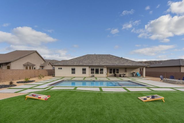 Back of the home with pool, lawn and cornhole boards