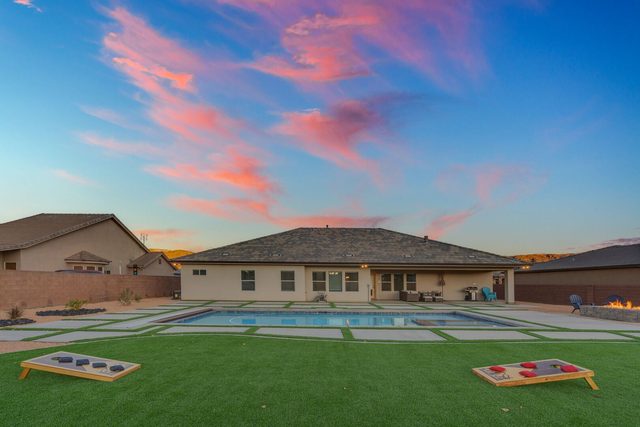 Rear view of the house with pool and cornhole lawn at sunset