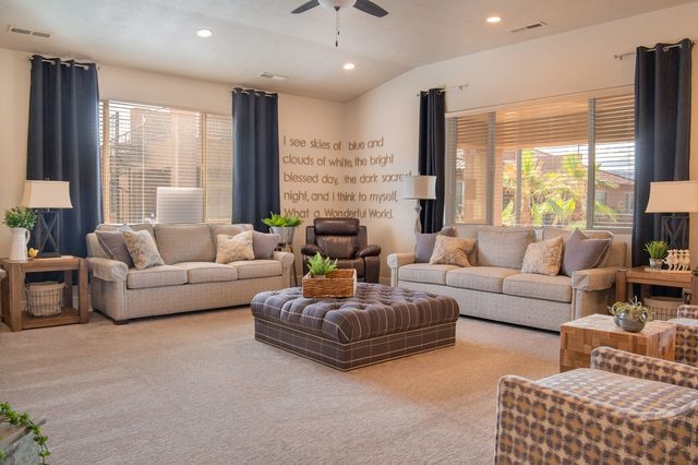 Living room seating with sofas and tufted ottoman under large windows