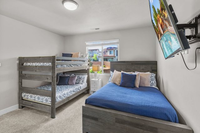 Bedroom with wood bunk bed, queen bed and wall-mounted TV