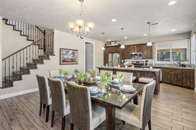 Dining table with upholstered chairs below chandelier near staircase