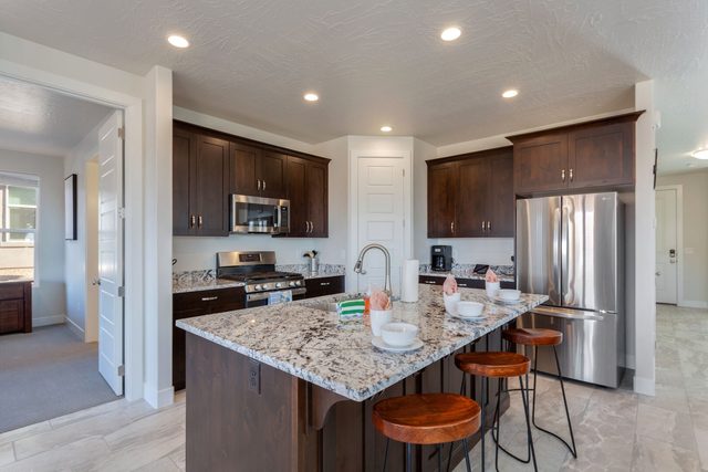 Kitchen with granite island, bar stools and stainless refrigerator