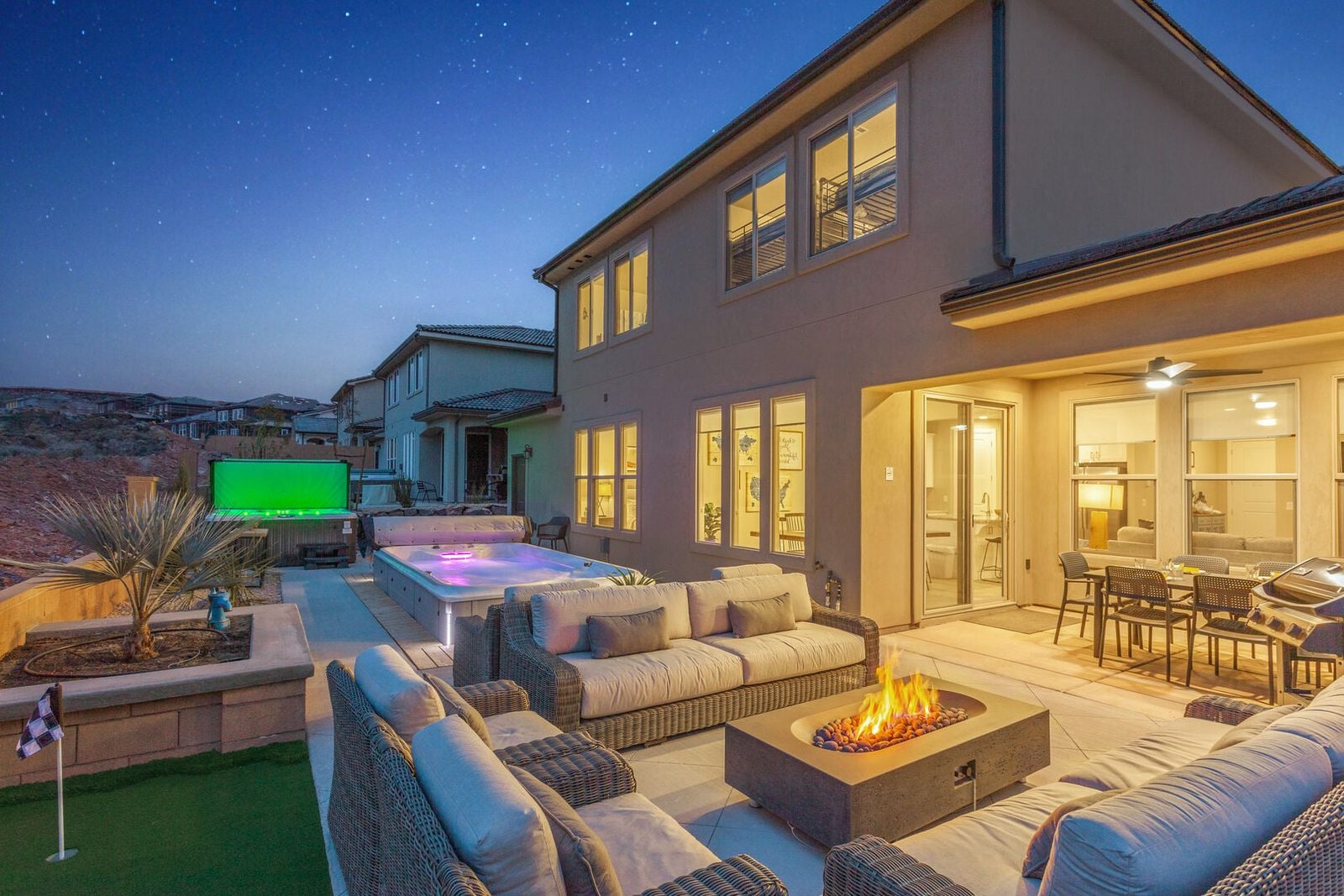 Backyard at dusk with fire pit lounge, spa and putting green at Paseos 1149
