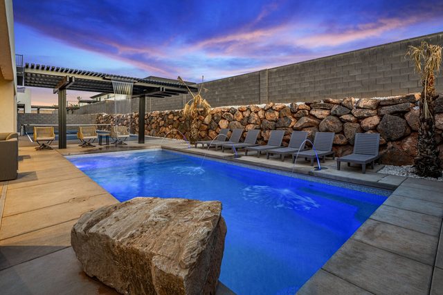 Lit private pool with loungers and pergola at dusk