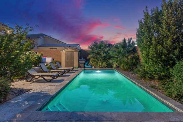 Lit private pool lined with lounge chairs at twilight