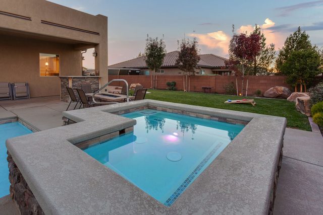 Lit private hot tub beside the pool at dusk