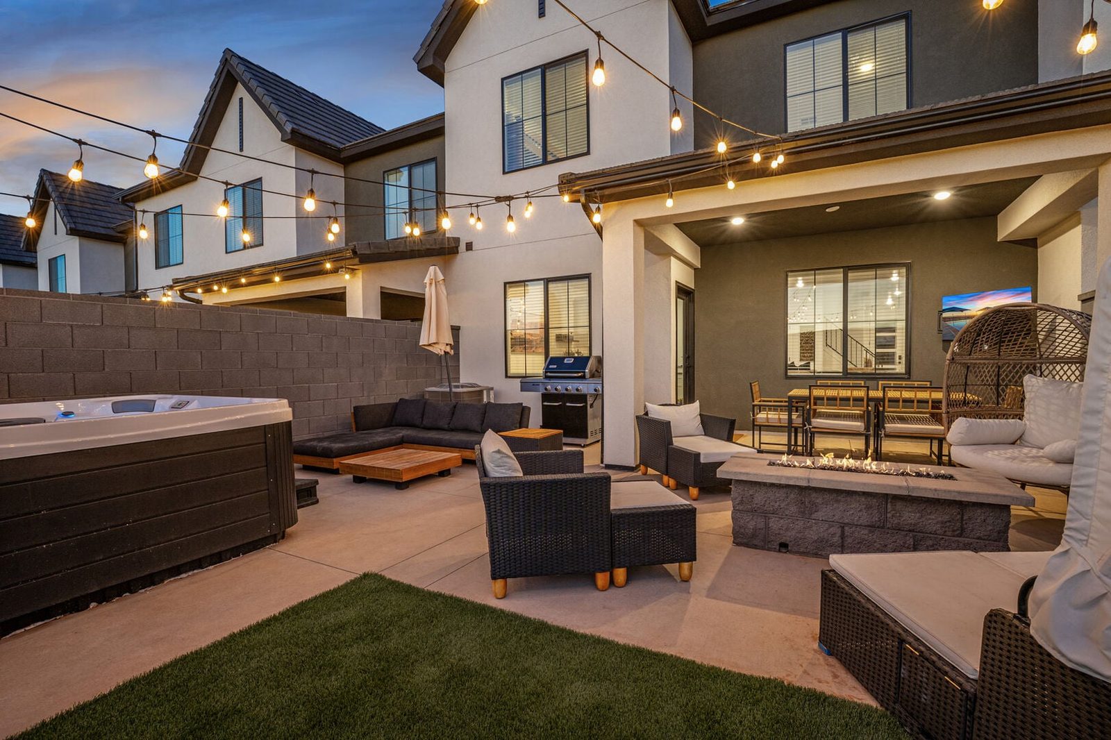 Backyard at dusk with hot tub, fire pit and string lights at Skyline 1690