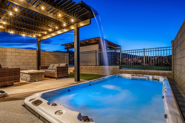 Lit private swim spa beside the pergola in the evening