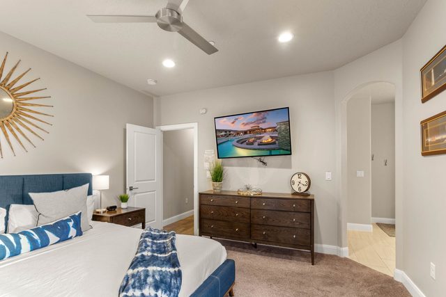 King bedroom with dresser, wall TV and ceiling fan