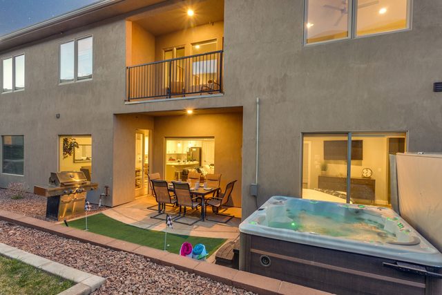 Rear exterior with balcony, lit patio and hot tub at dusk