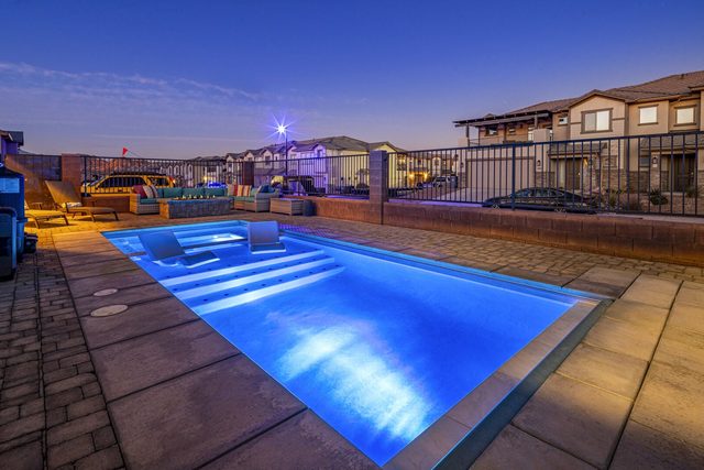 Private pool with lit water and lounge chairs at dusk