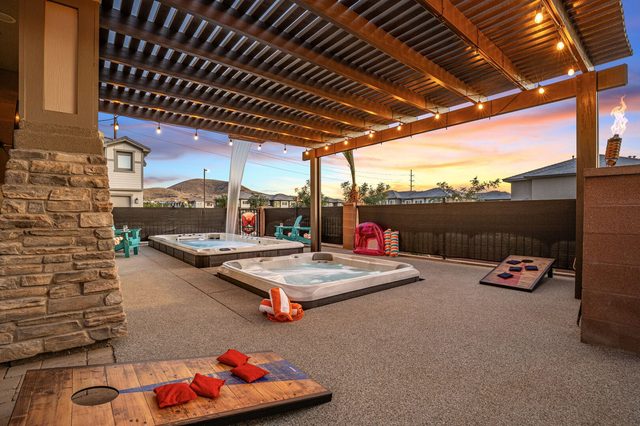 Backyard pergola with hot tub, swim spa and cornhole at sunset