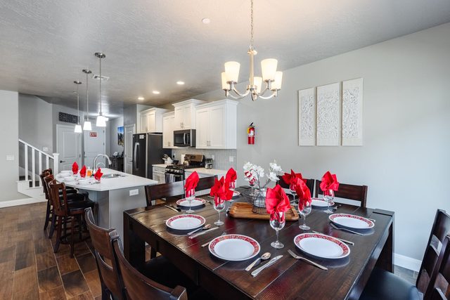 Dining table under chandelier with kitchen island beyond